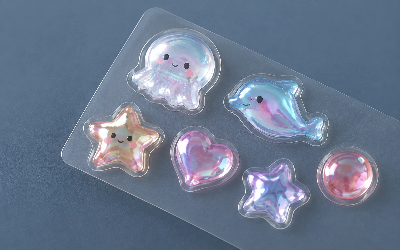 Six iridescent dimensional stickers with rainbow reflections on clear backing.