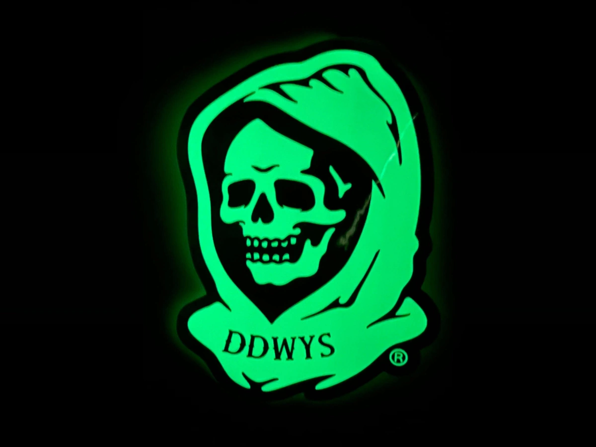 Custom die-cut glow-in-the-dark sticker glowing bright green in darkness